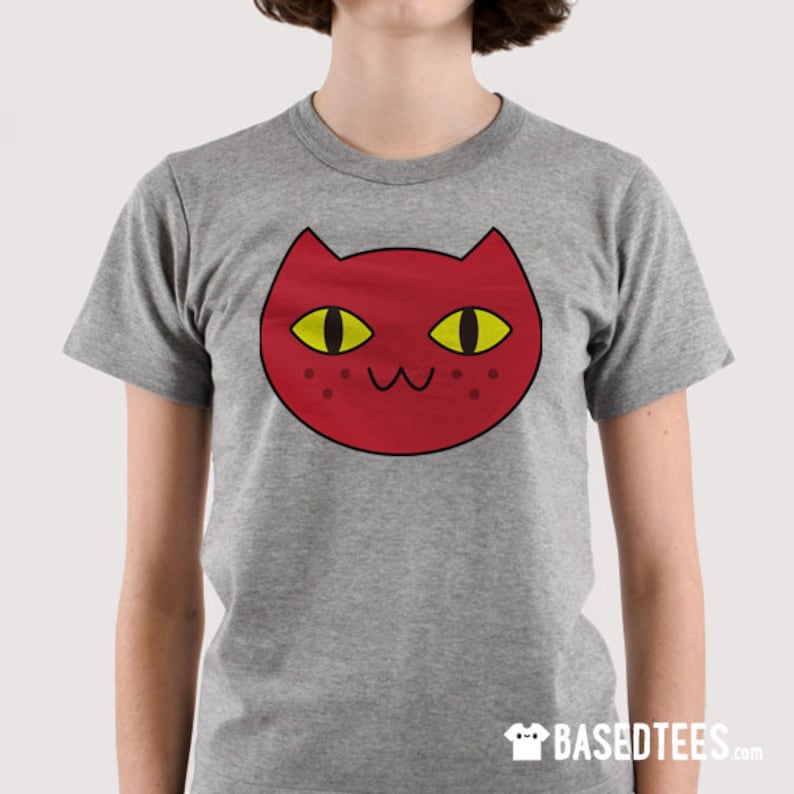 May include: A gray t-shirt with a red cartoon cat face with yellow eyes. The cat has a cute expression with a small smile and closed eyes.