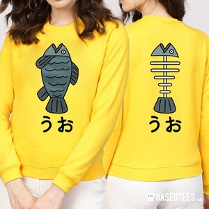 May include: Yellow sweatshirt with a cartoon fish on the front and a fish skeleton on the back. The text "うお" is printed below each image.
