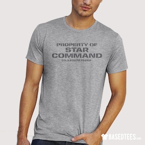 Op de afbeelding: Een grijs t-shirt met de tekst "PROPERTY OF STAR COMMAND ID:12007276289" gedrukt op de voorkant.