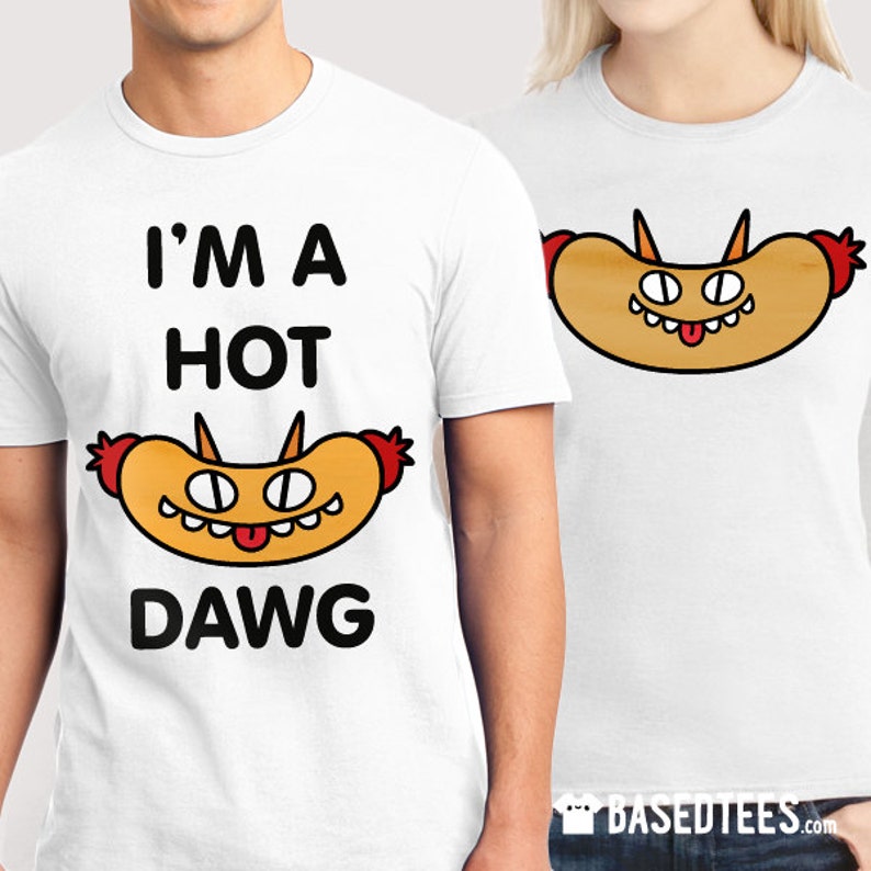 May include: White t-shirts with a cartoon hot dog graphic. One shirt reads "I'M A HOT DAWG" in black text. The hot dog illustration has a smiling face, horns, and red accents. The other shirt features the hot dog graphic.