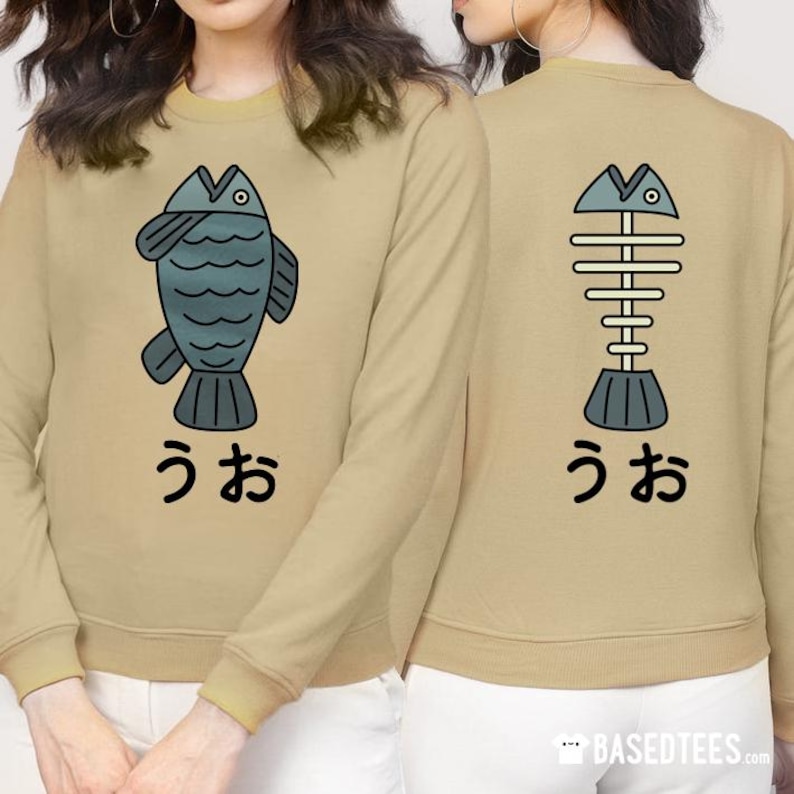 May include: A tan long-sleeved sweatshirt with a graphic of a blue fish on the front and a graphic of a fish skeleton on the back. The text "うお" is printed below each graphic.
