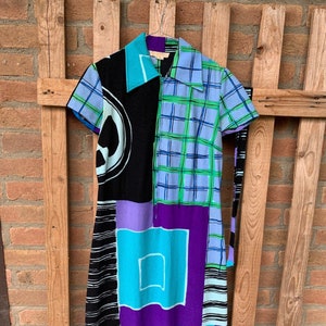 Puede incluir: Un vestido colorido con estampado geom&eacute;trico, manga corta y cuello. El vestido est&aacute; hecho de una tela ligera y tiene un lazo en la cintura.