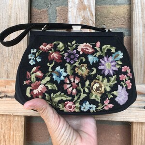 Può includere: Una borsa da sera in velluto nero con un ricamo floreale. Il ricamo presenta una varietà di fiori colorati, tra cui rosa, blu, viola e verde.