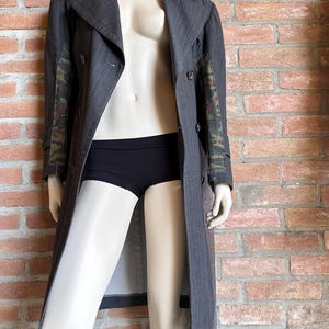May include: A gray pinstripe trench coat with camouflage patterned sleeves is displayed on a mannequin. The coat is buttoned and has a wide collar. The mannequin is also wearing black underwear.