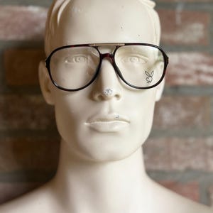 May include: A pair of brown and gold aviator glasses with a Playboy bunny logo on the right lens.