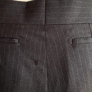 Peut inclure: Gros plan du dos d'un pantalon &agrave; fines rayures gris fonc&eacute;. Le tissu pr&eacute;sente des rayures blanches verticales. Le pantalon a deux poches arri&egrave;re et une couture au centre. La ceinture est visible en haut.