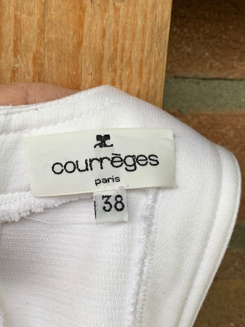 Puede incluir: Etiqueta de tela blanca con el nombre de la marca "courr&egrave;ges paris" en fuente negra. Debajo del nombre de la marca est&aacute; el n&uacute;mero "38" en fuente negra. La etiqueta est&aacute; adherida a tela blanca.