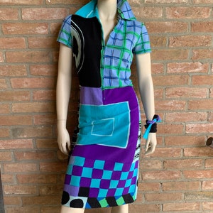 Puede incluir: Un vestido de manga corta con un patr&oacute;n geom&eacute;trico en tonos de azul, morado, negro y verde. El vestido tiene una cremallera y un cuello.
