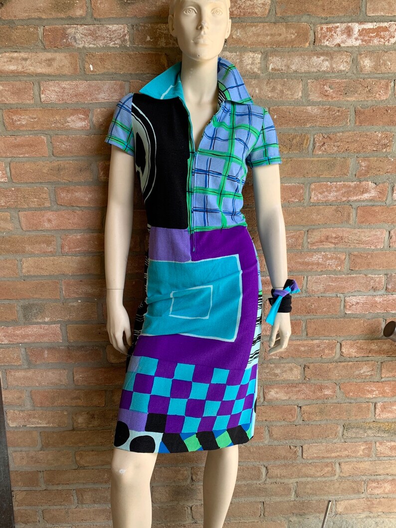 Puede incluir: Un vestido de manga corta con un patr&oacute;n geom&eacute;trico en tonos de azul, morado, negro y verde. El vestido tiene una cremallera y un cuello.