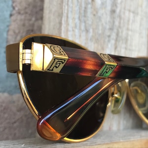 Può includere: Occhiali da sole aviator dorati con aste in tartaruga marrone. Le aste hanno dettagli dorati con le lettere "GF" su entrambi i lati.