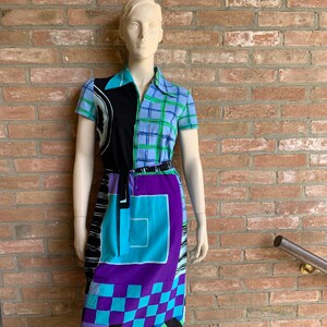 Puede incluir: Un vestido estampado en azul, negro, verde y morado con cuello y mangas cortas. El vestido tiene un dise&ntilde;o geom&eacute;trico y un cintur&oacute;n.