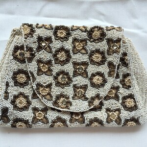 Può includere: Una pochette vintage con perline. La borsa presenta un motivo floreale nei toni del bianco, marrone e beige. La chiusura è un lembo arrotondato. Le piccole perline creano una superficie strutturata. La borsa è probabilmente della metà del XX secolo.