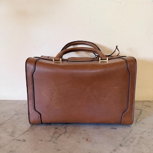 Estuche de tocador vintage Gucci de piel color camel con cierre giratorio y llave, herrajes dorados y escudo monogramado. Años 70. Hecho en Italia. De segunda mano. Excelente estado.