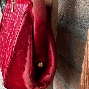 Pu&ograve; includere: Una borsa a mano in velluto rosso intenso con un motivo testurizzato sul davanti, una chiusura a telaio in metallo dorato e un manico in velluto abbinato. Il lato della borsa &egrave; fissato con un piccolo rivetto in metallo dorato e tessuto.