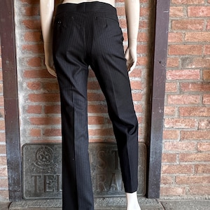 Peut inclure: Pantalon &agrave; fines rayures noires pr&eacute;sent&eacute; sur un mannequin. Le pantalon a une coupe classique et ajust&eacute;e, avec une jambe droite et de fines rayures. Le pantalon est en tissu fonc&eacute;, probablement de la laine ou un m&eacute;lange, et comporte une fermeture &agrave; bouton et &agrave; glissi&egrave;re.