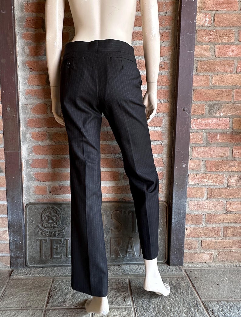 Peut inclure: Pantalon &agrave; fines rayures noires pr&eacute;sent&eacute; sur un mannequin. Le pantalon a une coupe classique et ajust&eacute;e, avec une jambe droite et de fines rayures. Le pantalon est en tissu fonc&eacute;, probablement de la laine ou un m&eacute;lange, et comporte une fermeture &agrave; bouton et &agrave; glissi&egrave;re.