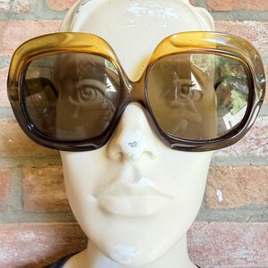 May include: Oversized sunglasses featuring a thick, translucent amber-brown plastic frame with a rounded, square-like shape. The lenses are tinted in a matching brown gradient, providing a cohesive look across the entire eyewear piece.