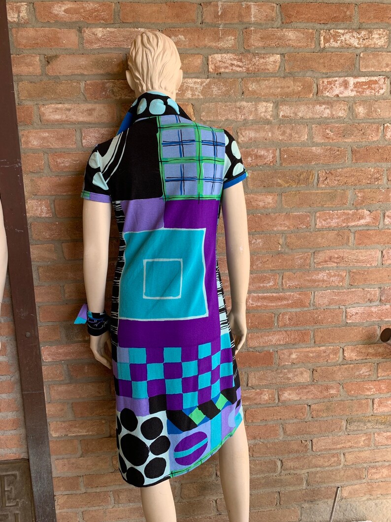 Puede incluir: Un vestido de manga corta con un patr&oacute;n geom&eacute;trico en tonos de azul, morado, negro y verde. El vestido tiene un cuello y una silueta ajustada.