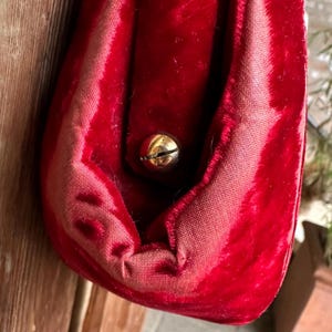 Pu&ograve; includere: Una pochette in velluto rosso intenso caratterizzata da una consistenza morbida e vellutata e da una silhouette arrotondata. La borsa &egrave; chiusa da un singolo bottone a pressione in metallo dorato lucido centrato sulla patta anteriore.