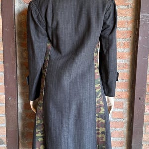 May include: A dark gray pinstripe coat with camouflage side panels. The long coat has a notched lapel, long sleeves, and a tailored fit. The camouflage pattern features shades of green, brown, and tan.