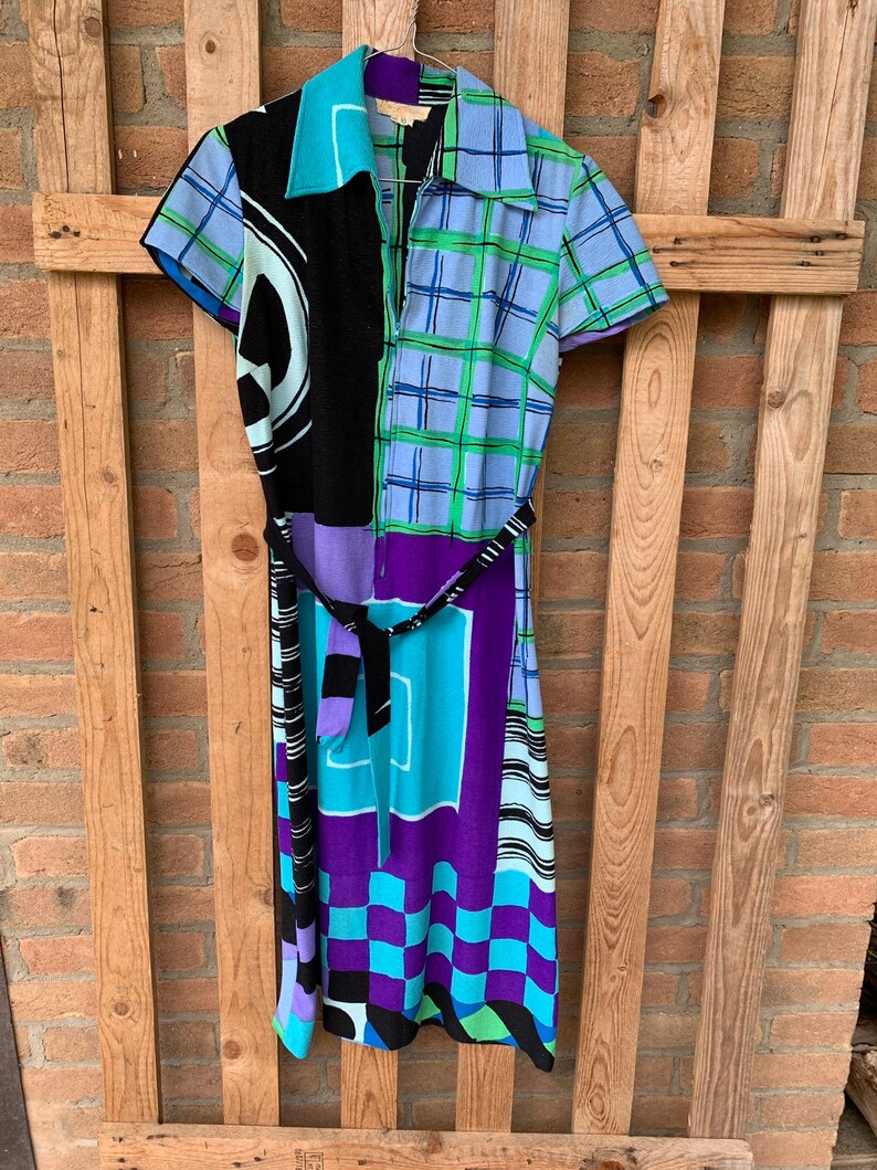 Puede incluir: Un vestido colorido con estampado geom&eacute;trico y cintur&oacute;n negro. El vestido tiene cuello y mangas cortas. El estampado incluye negro, azul, verde, morado y blanco.