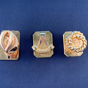 Può includere: Tre gemelli dorati, ognuno con un design diverso. Il primo gemello presenta un design a corda intrecciata, il secondo gemello presenta un design a corda semplice e il terzo gemello presenta un design a corda circolare.