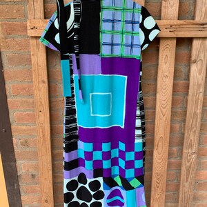 Puede incluir: Un vestido estampado con un dise&ntilde;o geom&eacute;trico colorido en negro, blanco, azul, verde y morado. El vestido tiene manga corta y un lazo en el cuello.
