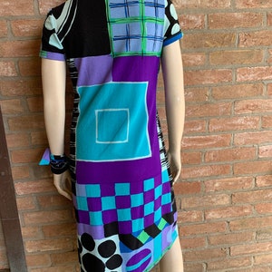 Puede incluir: Un vestido de manga corta con un patr&oacute;n geom&eacute;trico en tonos de negro, azul, morado y verde. El vestido tiene un cuello y una silueta ligeramente ajustada.