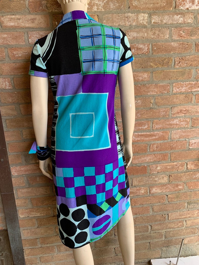 Puede incluir: Un vestido de manga corta con un patr&oacute;n geom&eacute;trico en tonos de negro, azul, morado y verde. El vestido tiene un cuello y una silueta ligeramente ajustada.