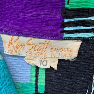 Puede incluir: Un primer plano de una etiqueta de ropa con el texto "Ken Scott Bandura Hand Printed in Italy" y el n&uacute;mero "10". La etiqueta est&aacute; unida a una tela con estampado azul, verde, morado y negro.