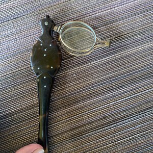 May include: A tortoiseshell magnifying glass with a silver frame and a handle. The handle is decorated with white dots.