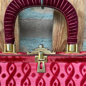 Pu&ograve; includere: Una borsa con manico in velluto rosso intenso con nervature verticali e corpo in velluto abbinato con un motivo ripetitivo di anelli e punti in velluto in rilievo. La borsa include una chiusura e finiture in metallo color oro.