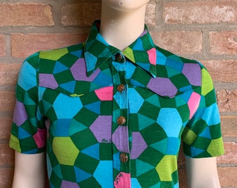 May include: A short-sleeved button-down shirt with a geometric pattern in shades of green, blue, pink, and purple. The shirt has a collar and a button closure.
