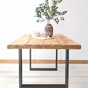 May include: A rustic wooden dining table with a natural wood finish and black metal legs. The table is set with two clear glass cups and a white plate.