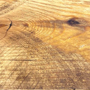Op de afbeelding: Close-up van een lichtbruin houten oppervlak met een knoop en nerfpatronen. Het hout heeft een natuurlijke, rustieke uitstraling.