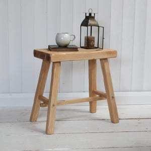 May include: A natural wood stool with a simple design. The stool has four legs and a rectangular top. It is made of light wood and has a rustic look.