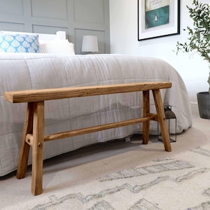 Op de afbeelding: Een rustieke houten bank met een natuurlijke afwerking. De bank heeft een eenvoudig ontwerp met twee poten aan elke kant en een enkele dwarsbalk die de poten verbindt. De bank is gemaakt van gerecycled hout en heeft een verweerde uitstraling.