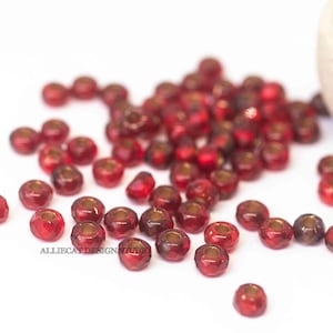 May include: A pile of small, red, faceted glass beads with gold-colored metal accents. The beads are scattered on a white surface.