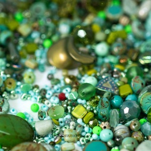 May include: A large assortment of green, blue and white glass beads of various shapes and sizes. The beads are scattered on a white surface.