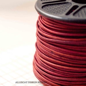 May include: A spool of red leather cord, wound tightly around a black plastic spool.