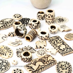 May include: An assortment of off-white carved beads and pendants with dark brown etched designs. The collection includes rings, cylinders, and flat pieces, featuring geometric and animal motifs. The beads are scattered on a white surface.