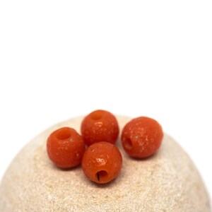 May include: Four orange coral beads on a light beige surface.