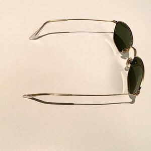 Peut inclure: Lunettes de soleil &agrave; monture dor&eacute;e avec des verres vert fonc&eacute;. Les lunettes ont une monture fine et d&eacute;licate.