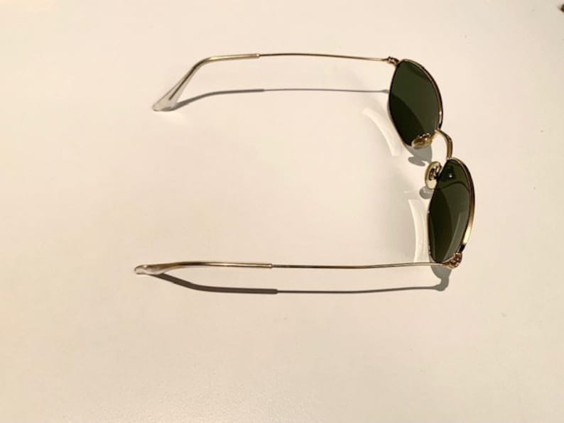 Peut inclure: Lunettes de soleil &agrave; monture dor&eacute;e avec des verres vert fonc&eacute;. Les lunettes ont une monture fine et d&eacute;licate.