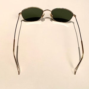 Peut inclure: Lunettes de soleil &agrave; monture dor&eacute;e avec des verres vert fonc&eacute;. Les lunettes ont une monture fine en m&eacute;tal et sont pr&eacute;sent&eacute;es de dos.