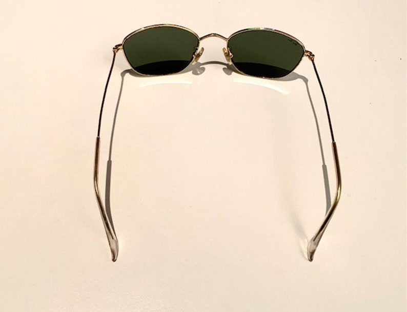 Peut inclure: Lunettes de soleil &agrave; monture dor&eacute;e avec des verres vert fonc&eacute;. Les lunettes ont une monture fine en m&eacute;tal et sont pr&eacute;sent&eacute;es de dos.
