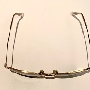 Peut inclure: Lunettes de soleil en m&eacute;tal dor&eacute; avec une monture fine et des verres rectangulaires. Les branches des lunettes sont fines et l&eacute;g&egrave;rement incurv&eacute;es.