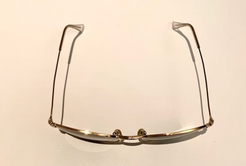 Peut inclure: Lunettes de soleil en m&eacute;tal dor&eacute; avec une monture fine et des verres rectangulaires. Les branches des lunettes sont fines et l&eacute;g&egrave;rement incurv&eacute;es.