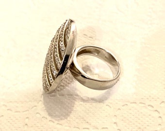 May include: A silver ring with a large, oval-shaped faceted stone set in a silver band. The stone is covered in small, clear crystals.