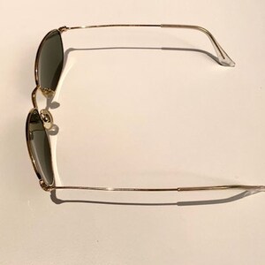 Peut inclure: Lunettes de soleil en m&eacute;tal dor&eacute; avec des verres vert fonc&eacute;. Les lunettes ont une monture fine en m&eacute;tal et sont de style classique.